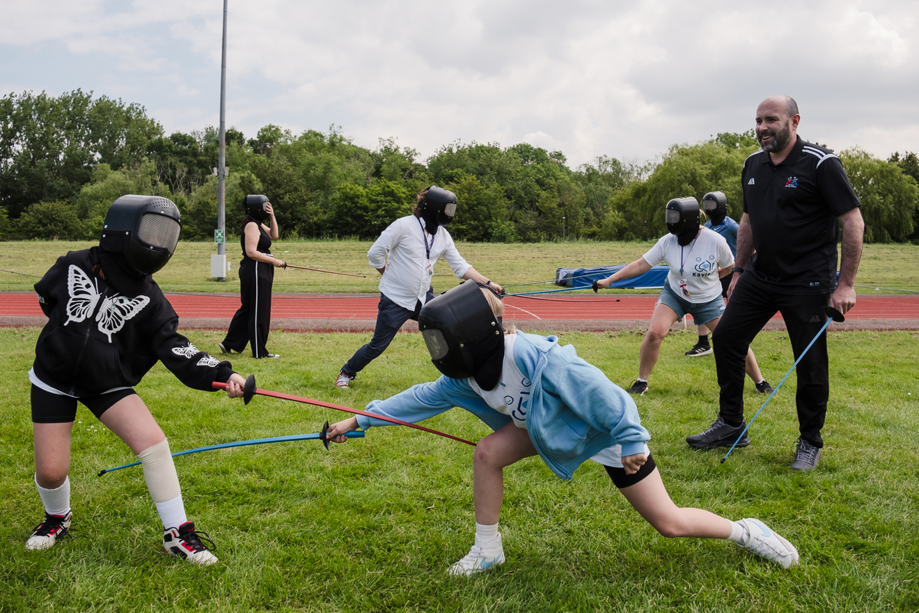 Young people trying out fencing with instructor looking on